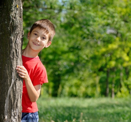 Portrait of cute boy standing near the tree in parkの写真素材