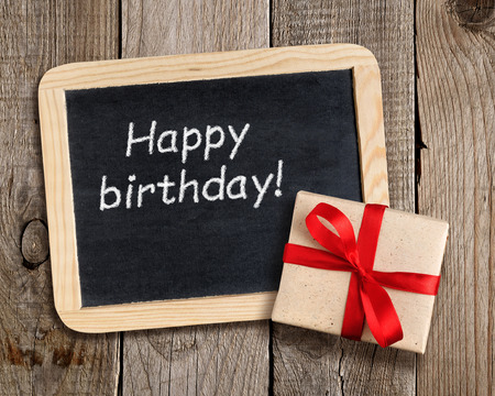 Blackboard with Happy birthday! phrase and gift box on wooden backgroundの写真素材