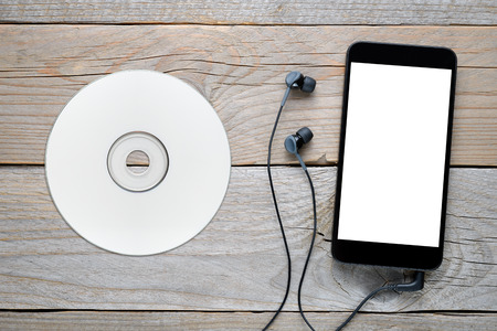 Smartphone with headphones and CD on wooden table
