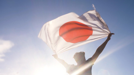 Young man holding spanish national flag to the sky with two hands at the beach at sunsetの写真素材