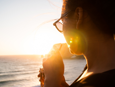 Young woman drinking cocktail at sunset in front of the sea on Ponza island coast