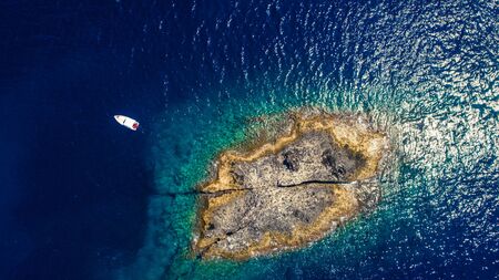 Aerial top view of a deserted island with white boat. Rocky shore of Zannone island near Ponza, Italy. Blue clear water on sunny day.の写真素材