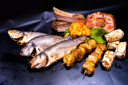 still life - meat with stuffed, shish kebab, steak in batter, crepes with fillings, fried fish on the black backgroundの写真素材