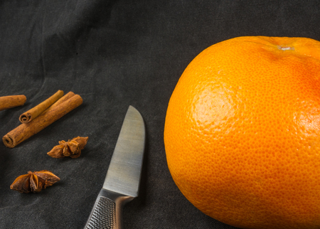 a large grapefruit with a knife, cinnamon sticks and star anise on a black textile backgroundの写真素材