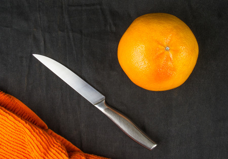 a large grapefruit with a knife and an orange napkin on a black textile backgroundの写真素材