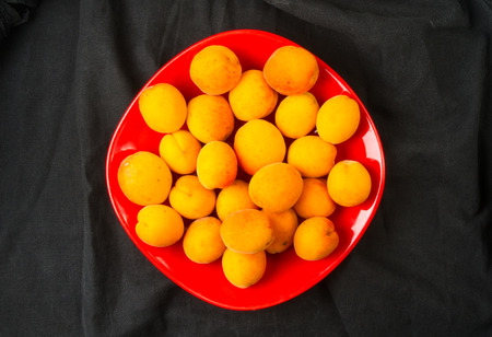 fresh ripe apricots in red plate on black background, closeupの写真素材