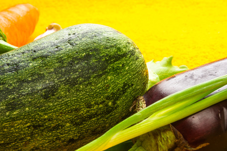 still life - carrots, onion, lettuce, cucumber, cilantro, eggplant and peppers on bright yellow backgroundの写真素材