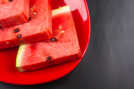 slices of ripe juicy watermelon in red plate on black background