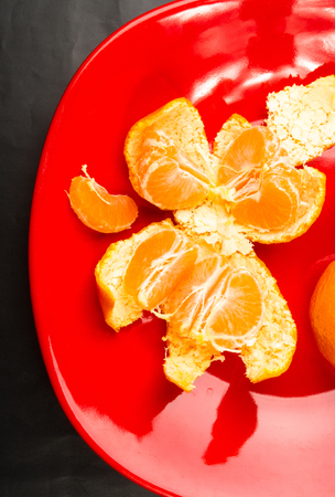 tangerines, peeled tangerine and tangerine slices in a red plate on black backgroundの写真素材