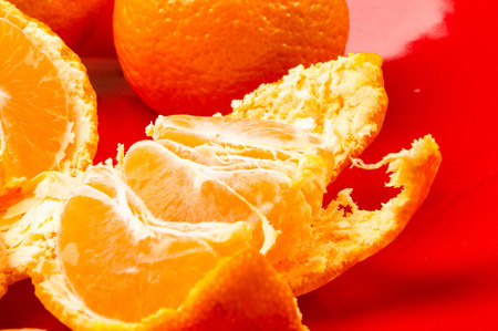 tangerines, peeled tangerine and tangerine slices in a red plate on black backgroundの写真素材