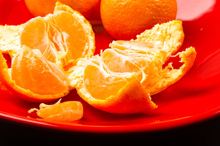 tangerines, peeled tangerine and tangerine slices in a red plate on black backgroundの写真素材