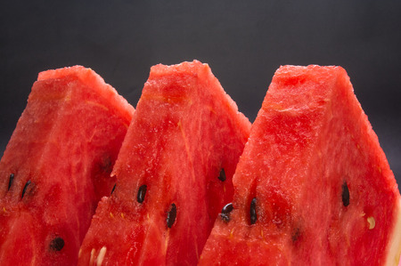 slices of ripe juicy watermelon in red plate on black backgroundの写真素材