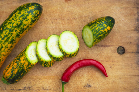 slices unusual green-orange zucchini and red chilly on an old wooden backgroundの写真素材