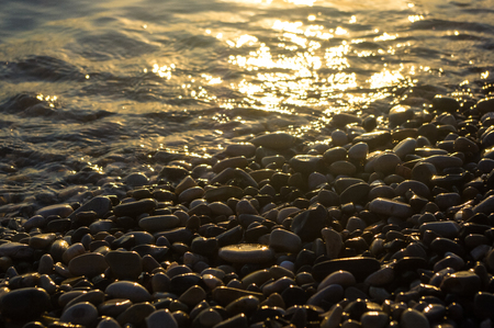 sea pebble beach with multicoloured stones, transparent waves with foam, on a warm eveningの写真素材