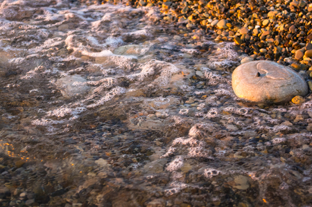 sea pebble beach with multicoloured stones, transparent waves with foam, on a warm eveningの写真素材