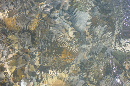 sea pebble beach with multicoloured stones, transparent waves with foam, on a warm summer day