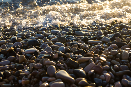 sea pebble beach with multicoloured stones, transparent waves with foam, on a warm eveningの写真素材