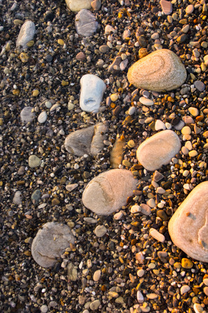 sea pebble beach with multicoloured stones, transparent waves with foam, on a warm evening