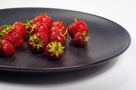 fresh ripe berries strawberries on black ceramic plate on white backgroundの写真素材