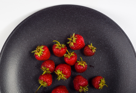 fresh ripe berries strawberries on black ceramic plate on white backgroundの写真素材