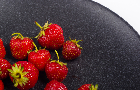 fresh ripe berries strawberries on black ceramic plate on white backgroundの写真素材