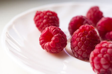 big fresh juicy raspberries on a white saucer close up, selected focus