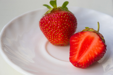 half of the cut fresh ripe berries strawberries on white plate, macro photoの写真素材