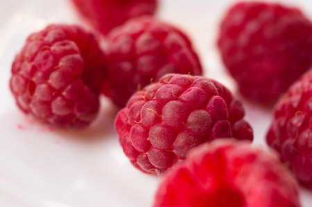 big fresh juicy raspberries on a white saucer close up, selected focusの写真素材