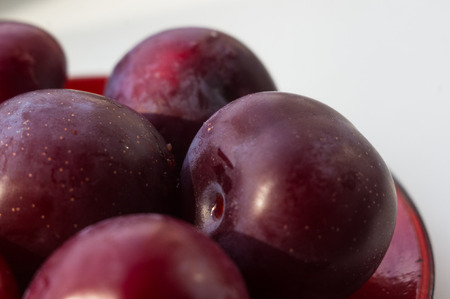 fresh plum fruit with cut plum slices in the red saucer on white background