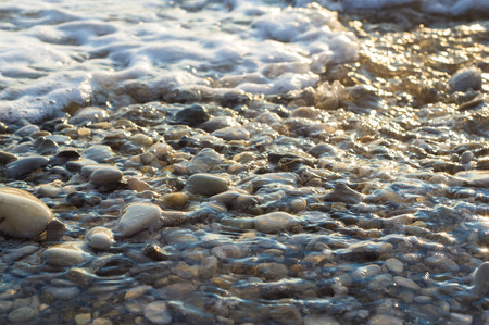 pebble stones on the sea beach on a warm summer day, the rolling waves of the blue sea with white foamの写真素材