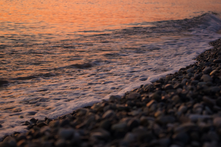 Summer sea sunset on the pebble beach, the sun, waves and clouds, beautiful dramatic lightingの写真素材