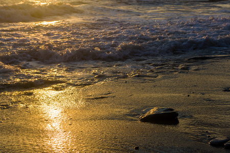 pebble stones on the sea beach on a warm summer day, the rolling waves of the blue sea with white foamの写真素材