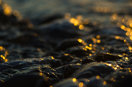 pebble stones on the sea beach on a warm summer day, the rolling waves of the blue sea with white foamの写真素材