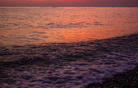 Summer sea sunset on the pebble beach, the sun, waves and clouds, beautiful dramatic lightingの写真素材