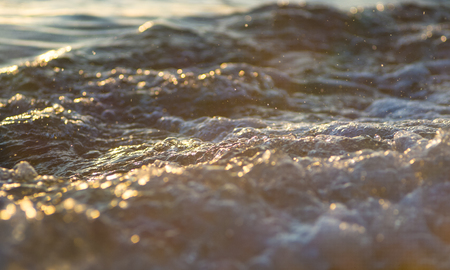 pebble stones on the sea beach on a warm summer day, the rolling waves of the blue sea with white foamの写真素材