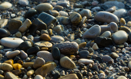 pebble stones on the sea beach on a warm summer day, the rolling waves of the blue sea with white foamの写真素材