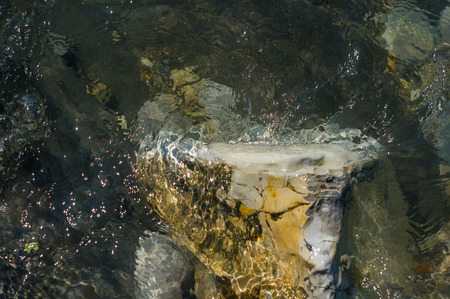 Pebble stones on the sea beach on a warm summer day, the rolling waves of the blue sea with white foamの写真素材