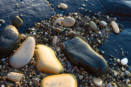 Pebble stones on the sea beach on a warm summer day, the rolling waves of the blue sea with white foamの写真素材