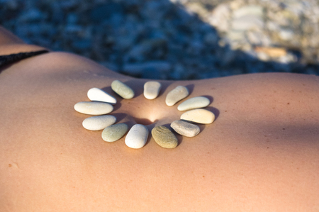 Pattern of small sea stones on women's skin, pebble beach on a hot summer dayの写真素材