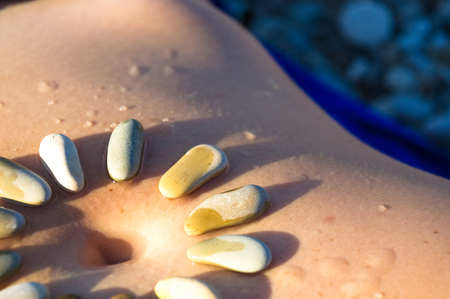 Pattern of small sea stones on women's skin, pebble beach on a hot summer dayの写真素材