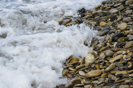 pebble stones on the sea beach on a warm summer day, the rolling waves of the blue sea with white foamの写真素材