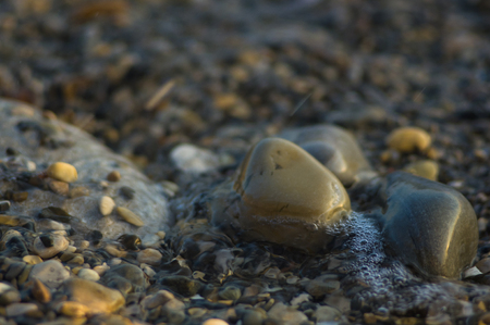 pebble stones on the sea beach on a warm summer day, the rolling waves of the blue sea with white foamの写真素材