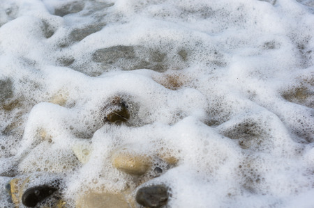 pebble stones on the sea beach on a warm summer day, the rolling waves of the blue sea with white foamの写真素材
