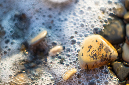 pebble stones on the sea beach on a warm summer day, the rolling waves of the blue sea with white foamの写真素材
