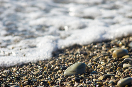 pebble stones on the sea beach on a warm summer day, the rolling waves of the blue sea with white foamの写真素材