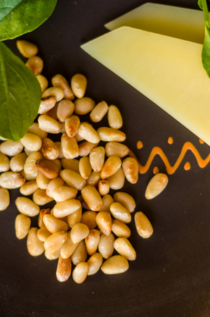 Fresh ingredients for preparing Italian pesto sauce - lemon basil sprigs, peeled seeds of cedar nuts, large garlic clove, Greek olive oil, Parmesan cheese, on a ceramic plate, in scattered sunlightの写真素材