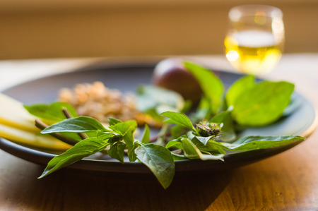 Fresh ingredients for preparing Italian pesto sauce - lemon basil sprigs, peeled seeds of cedar nuts, large garlic clove, Greek olive oil, Parmesan cheese, on a ceramic plate, in scattered sunlightの写真素材