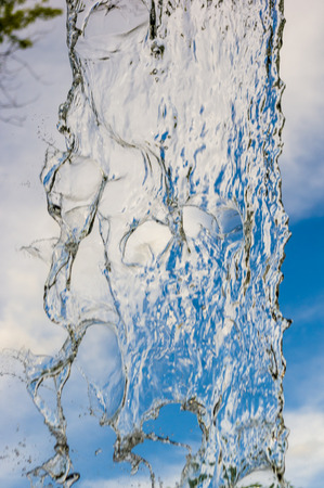 transparent falling water vertical flows against a blue sky and green landscape, close-upの写真素材
