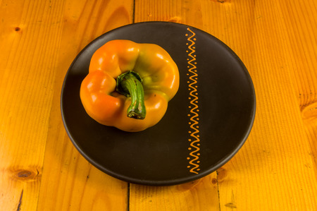 a freshest yellow paprika, bell pepper in ceramic plate on wooden background, close up