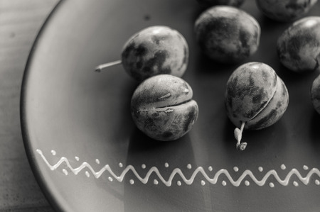 juicy blue plums in ceramic plate on wooden background, close-up